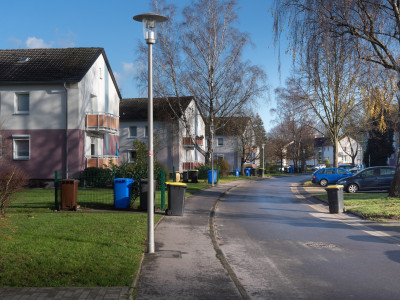 Foto einer Straße in einer Wohnsiedlung, Mehrfamilienhäuser, nasser Asphalt bei Sonnenschein