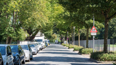 Straße mit parkenden Autos links und Hinweisschild auf spielende Kinder