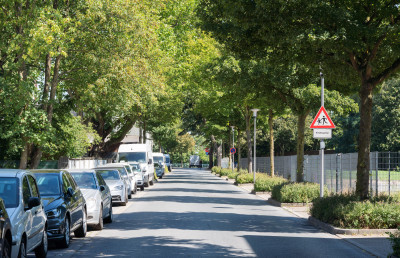 Straße mit parkenden Autos links und Hinweisschild auf spielende Kinder