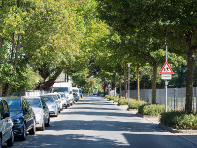 Straße mit parkenden Autos links und Hinweisschild auf spielende Kinder