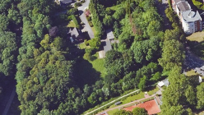 Luftaufnahme eines Stadtgebiets mit Häusern, Bäumen, einem Asche-Sportplatz und Fußwegen
